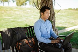 Man sitting on a park bench and working on a laptop